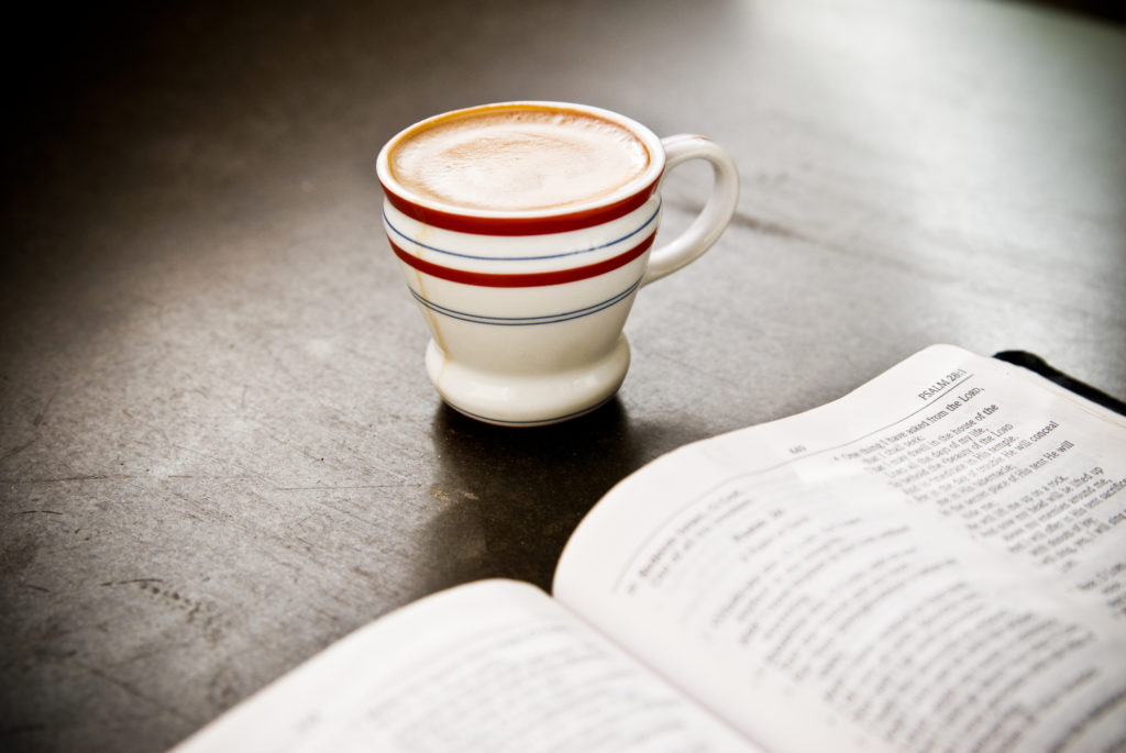 A double espresso sitting on the table next to a bible open to Psalms.